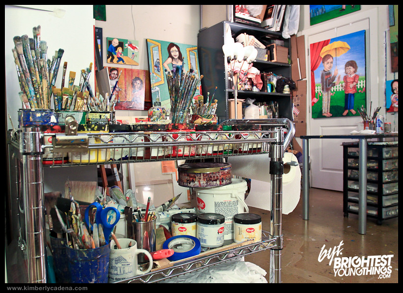 Brushes and paints on a cart, with paintings behind