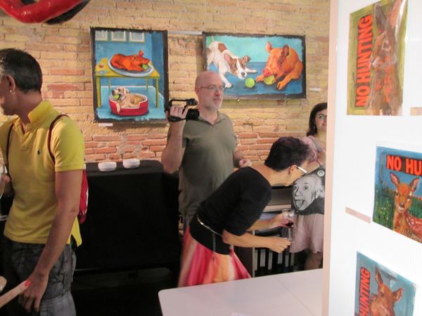 Visitors and a video camera in front of Dana Ellyn's animal paintings, some lettered NO HUNTING