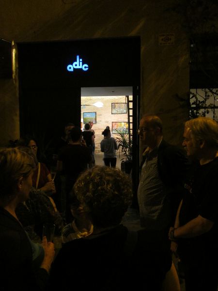 Visitors at the gallery doorway at night, looking in at the paintings