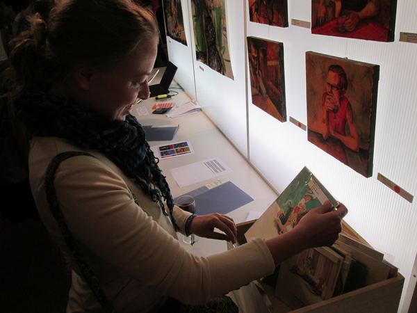 A visitor looking through prints at the white table in front of Dana Ellyn's portraits