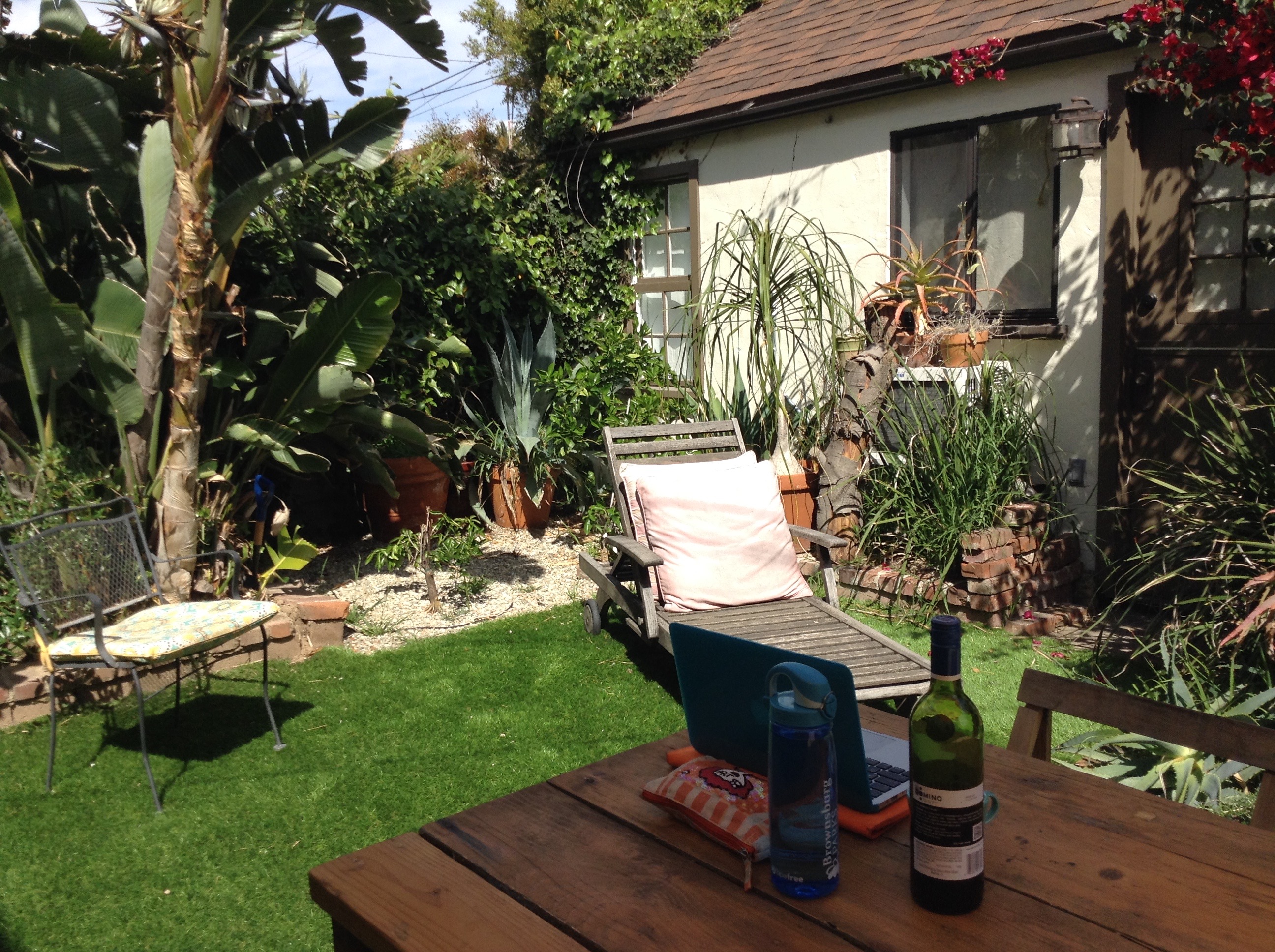 Sunny garden at a Los Angeles Airbnb, with a lounge chair, tropical plants and a laptop on a wooden table