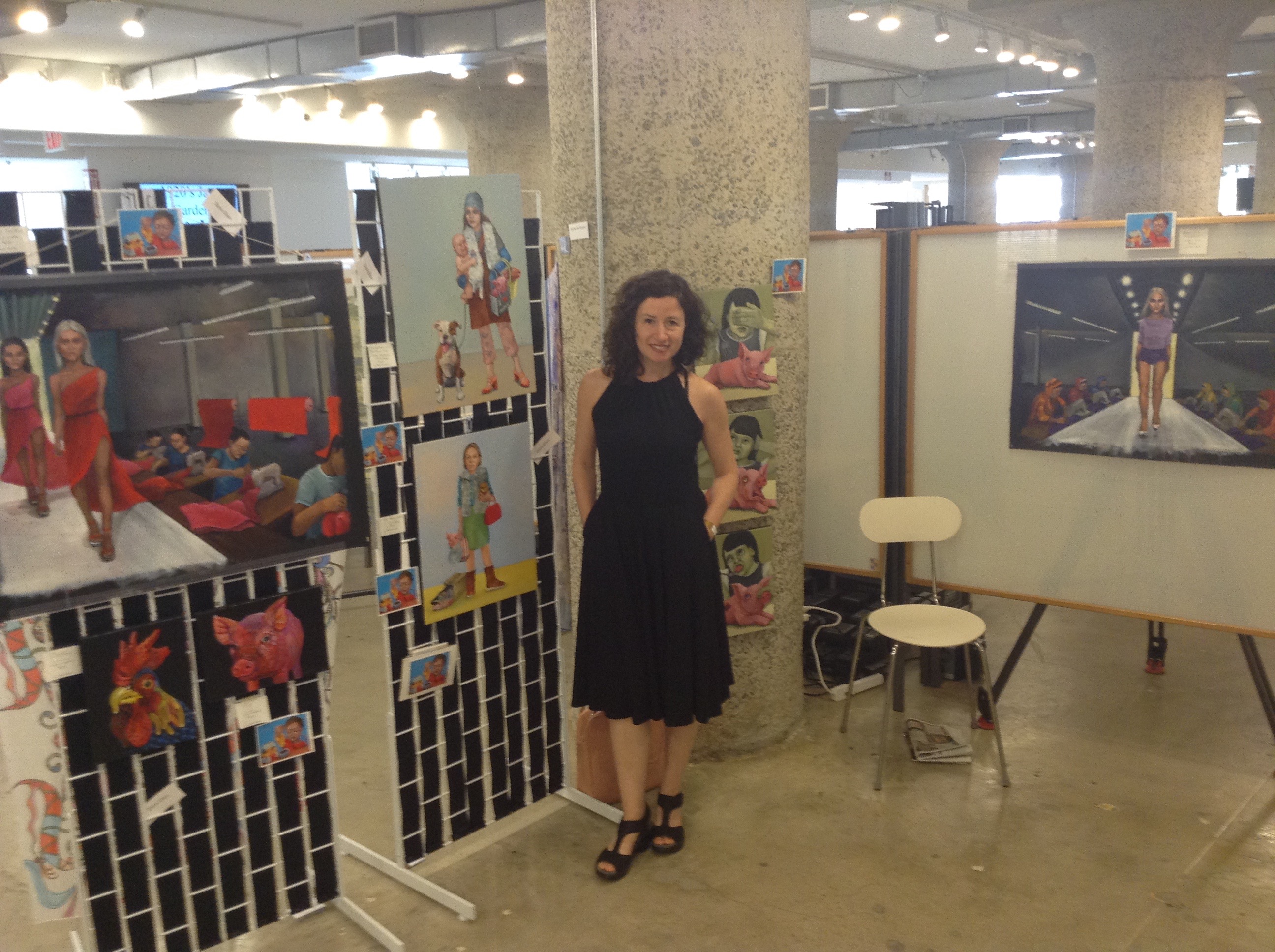 Dana Ellyn standing among her paintings at Moda 360, in a black dress