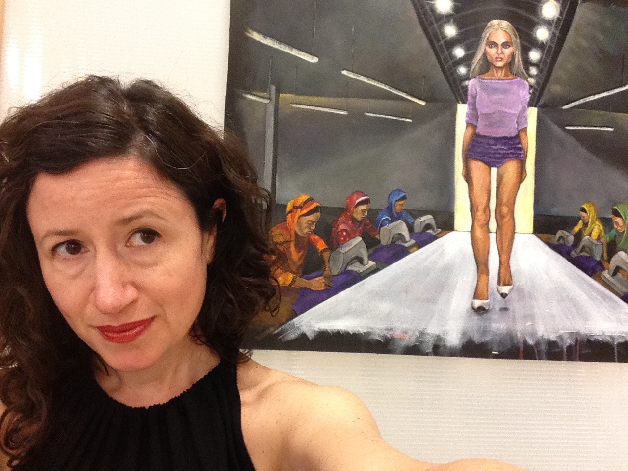 Dana Ellyn beside her painting Meet Your Makers, a model in purple on a runway with garment workers sewing on either side