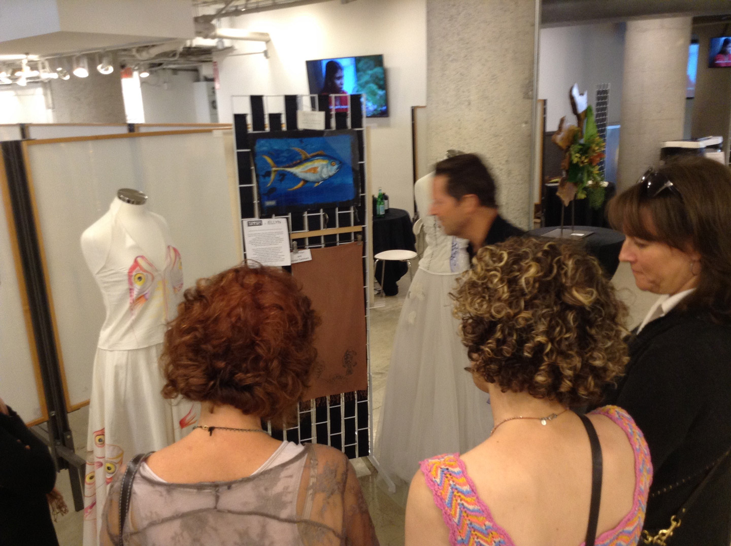 Visitors at Moda 360 looking at the Bycatch, By Hand dresses and Ellyn’s yellowfin tuna painting with Tammam’s stitching