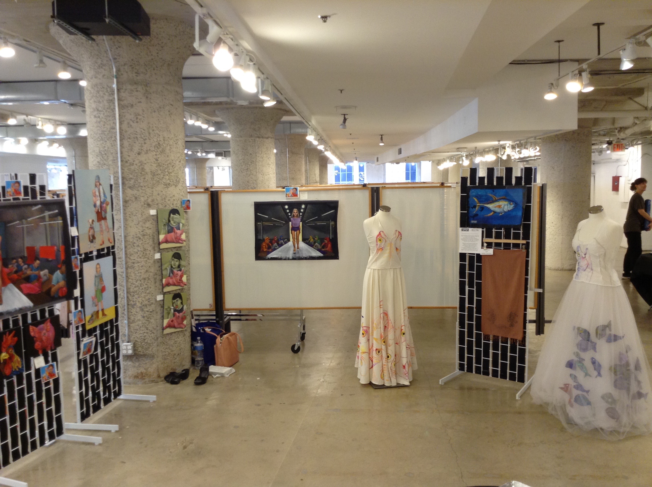Wide view of the Moda 360 hall showing Dana Ellyn’s paintings and the two Bycatch, By Hand dresses