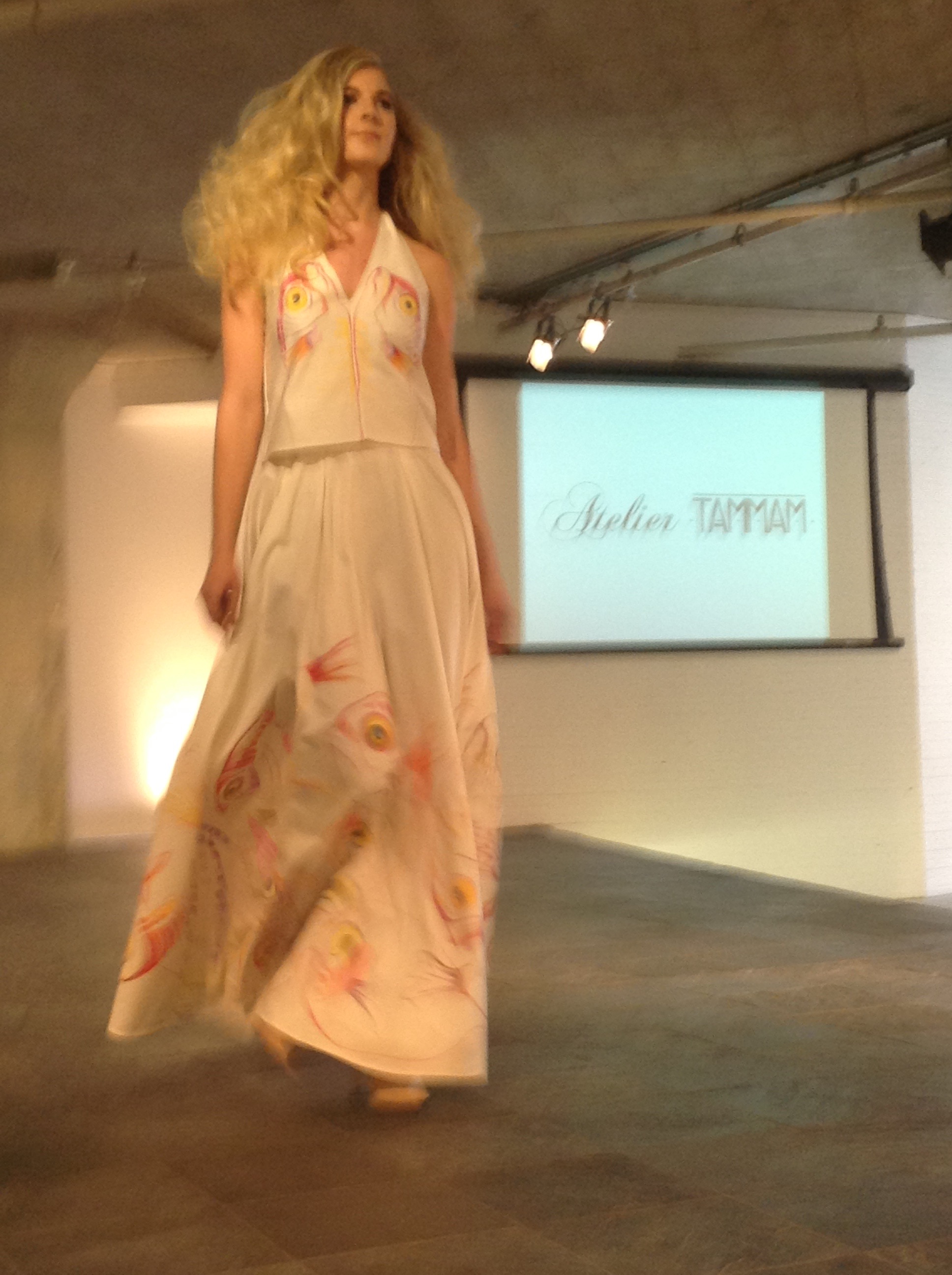 Model on the Moda 360 runway in the hand-painted Bycatch, By Hand dress, an Atelier Tammam screen behind her