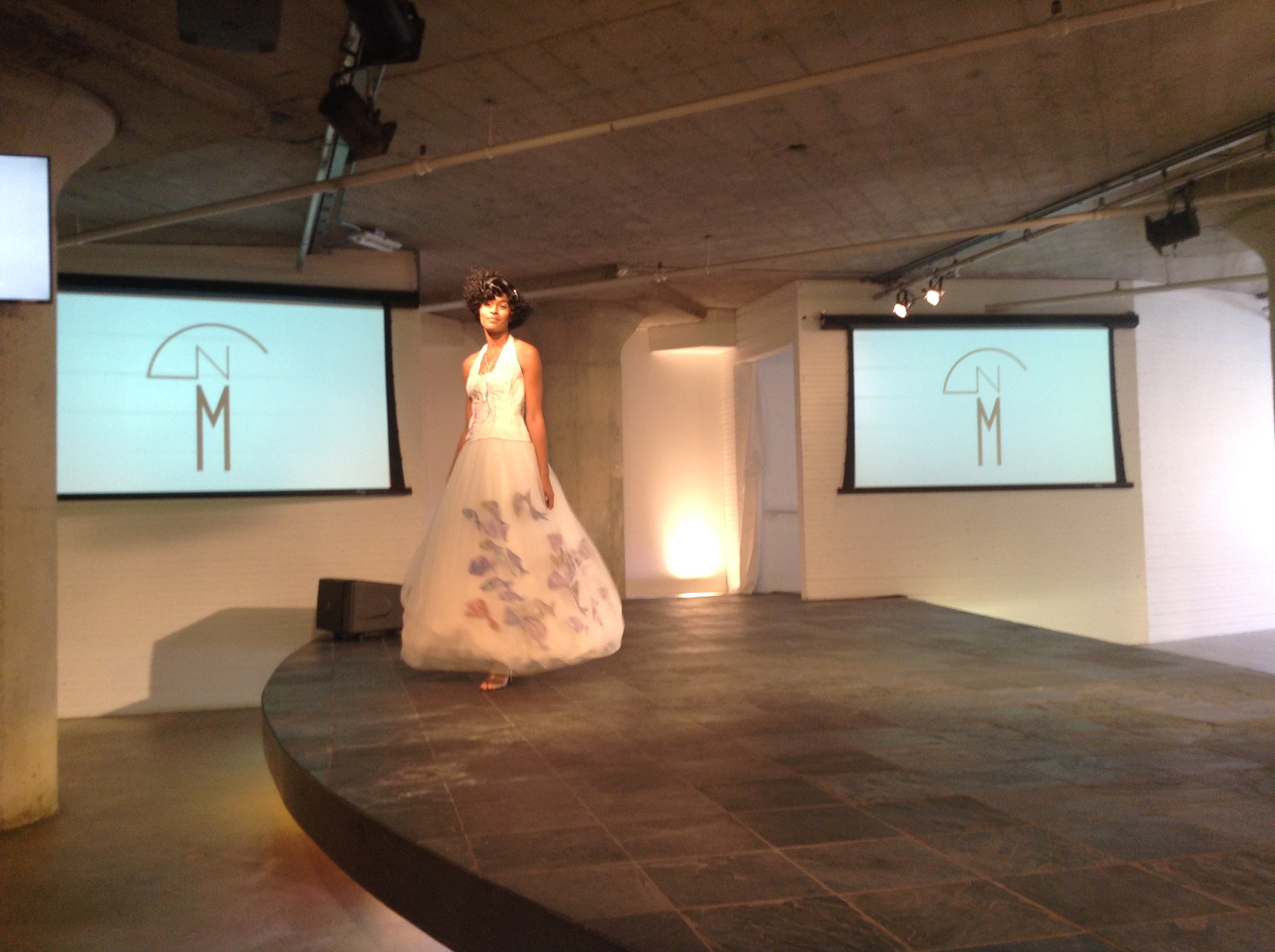 Model in the Bycatch, By Hand tulle gown on the Moda 360 stage between two screens showing The New Mart logo