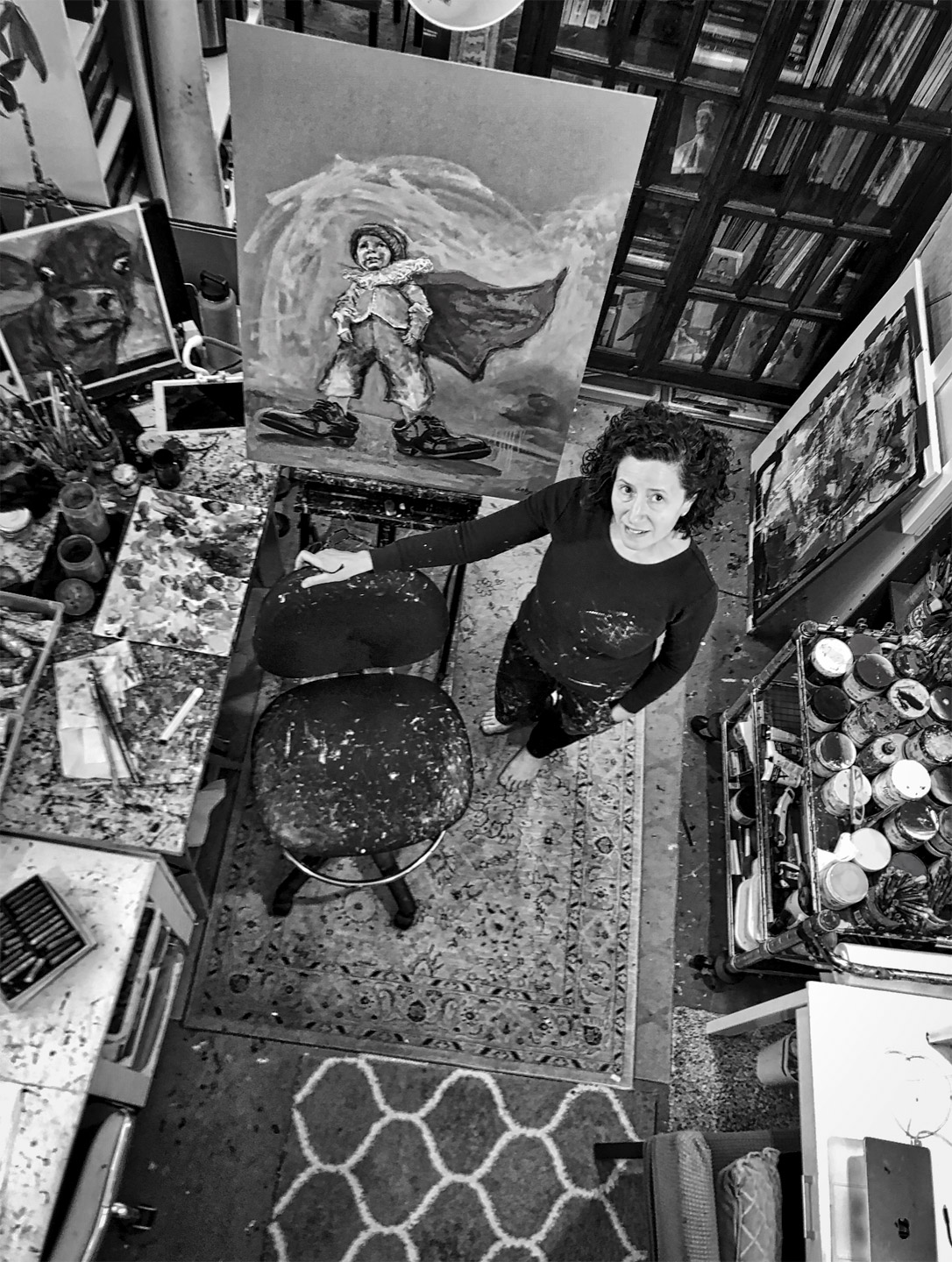 Dana Ellyn in her half of the studio at Mather Studios, painting on her easel, surrounded by canvases, paints, and art supplies